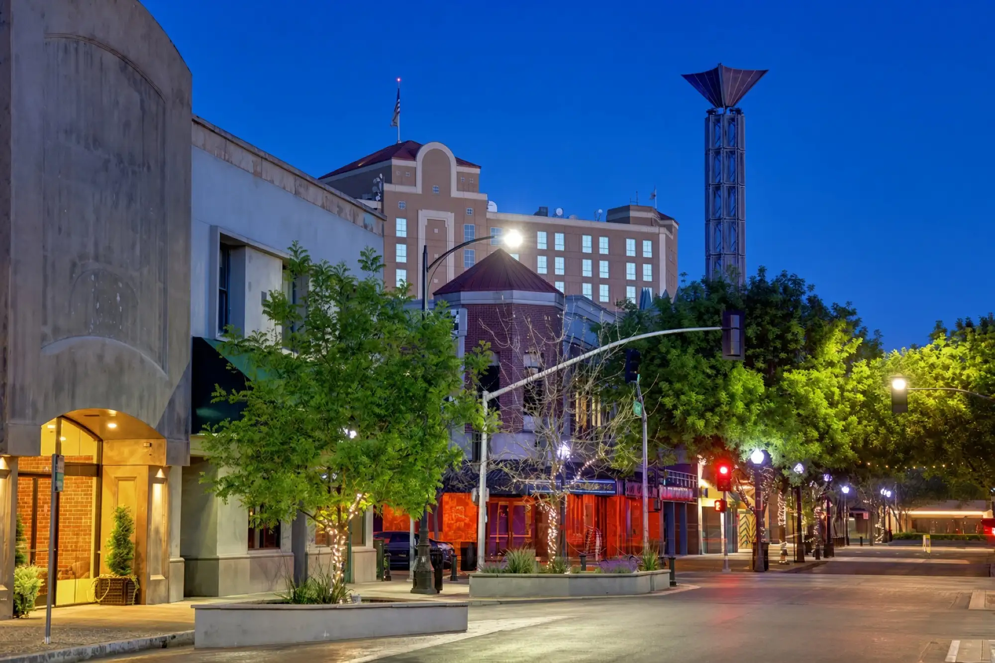 Una calle del centro de Modesto al anochecer con una torre iluminada y árboles
